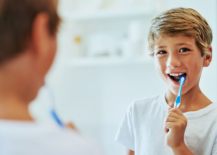 A young boy brushing his teeth in front of the mirror