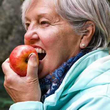 An elderly woman bitting on an apple