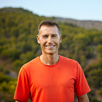 A man wearing an orange t-shirt smiling outdoors